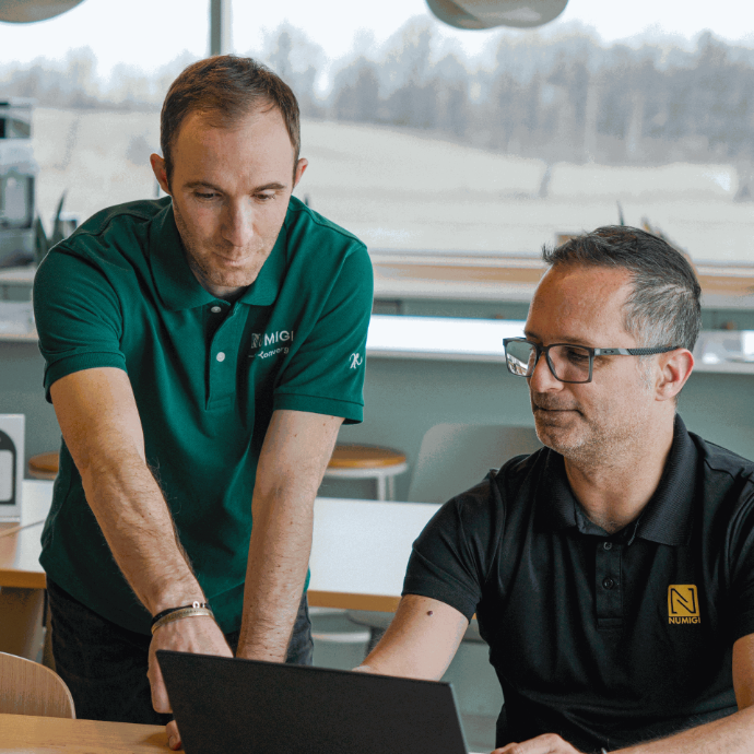 2 fondateurs de Numigi, Bruno Joliveau et Julien Jézéquel-Breard, experts en implémentation ERP, souriants en train de regarder l’écran d’un ordinateur portable dans les bureaux Hedhofis au Québec.